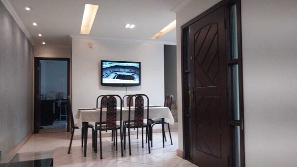 A dining area with a table and chairs, a television mounted on the wall, and a door. - House near Pampulha (Contagem)