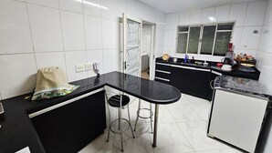 A compact kitchen with white tiled walls, a black countertop, and a small refrigerator. - House near Pampulha (Contagem)
