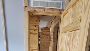 A hallway with wooden walls and doors, a ceiling vent, and a light switch on the wall.