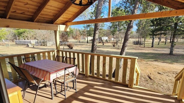A wooden deck with a table and chairs, surrounded by a wooden fence, overlooking a grassy area with trees.