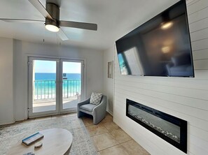 Una sala de estar moderna con un televisor grande, chimenea y vistas al océano a través de puertas de vidrio.