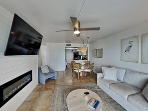 Una sala moderna con televisor de pantalla plana, ventilador de techo, chimenea, comedor con mesa y sillas, y sofá.