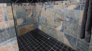 Un área de ducha con azulejos negros y de varios colores, un desagüe a la vista y una toalla colgada en la pared.