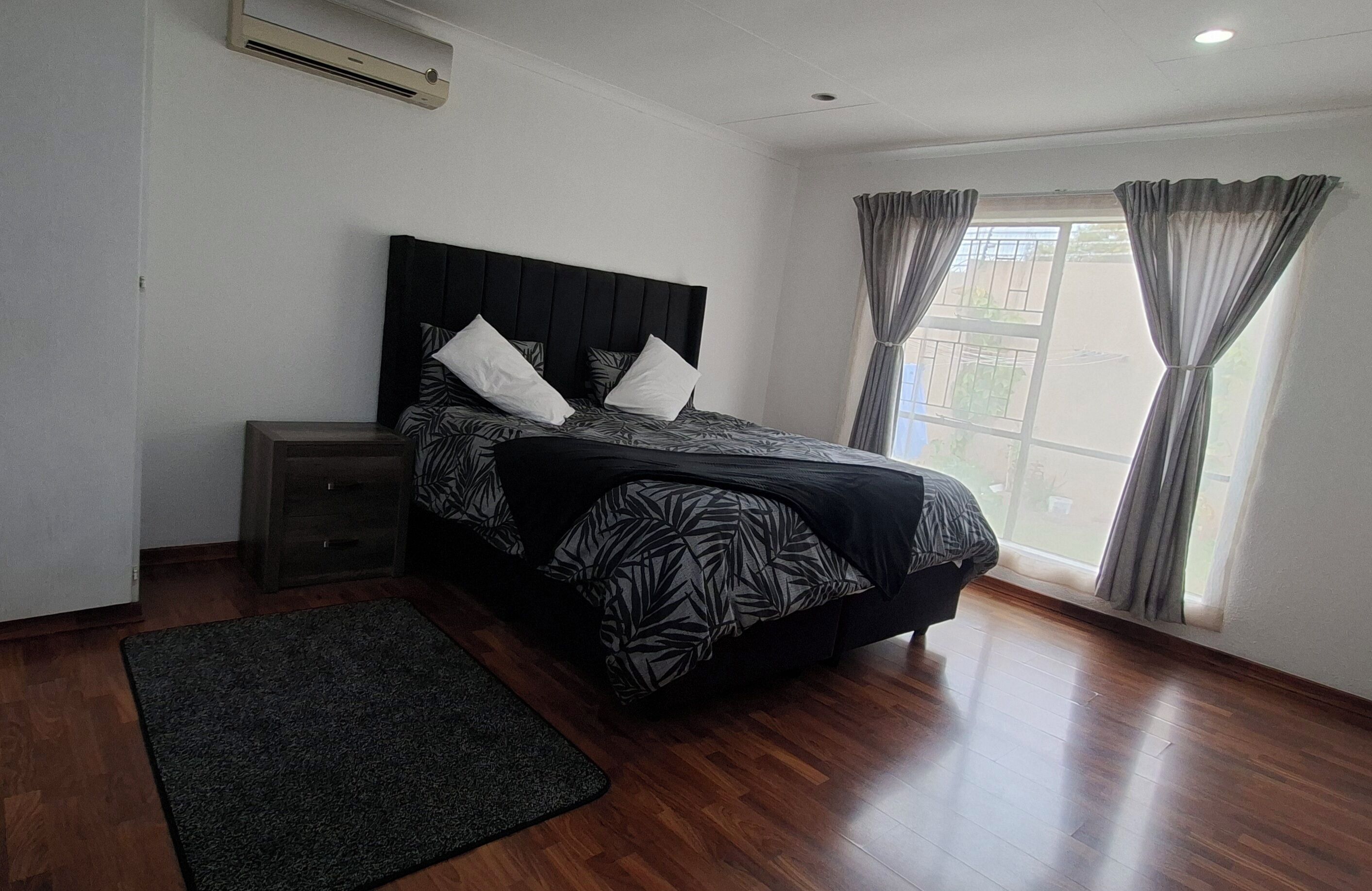 Une chambre à coucher avec un lit, une table de chevet, une fenêtre avec des rideaux et un plancher en bois.