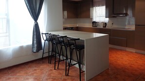 Una cocina moderna con una isla central, taburetes de bar y un ventanal con cortinas.