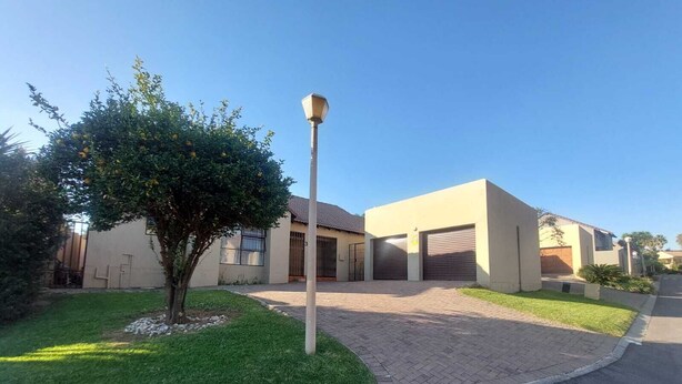 Un barrio residencial con una casa moderna que cuenta con garaje, entrada pavimentada y césped cuidado.