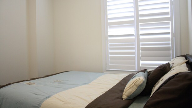 A bedroom with a bed, a window with blinds, and a plain wall.