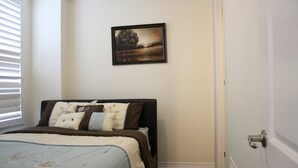 A bedroom with a bed, pillows, a framed picture on the wall, and a door.