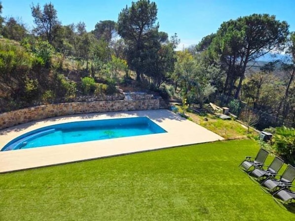 Une piscine bordée de pierres, entourée d’une pelouse bien entretenue et d’arbres.
