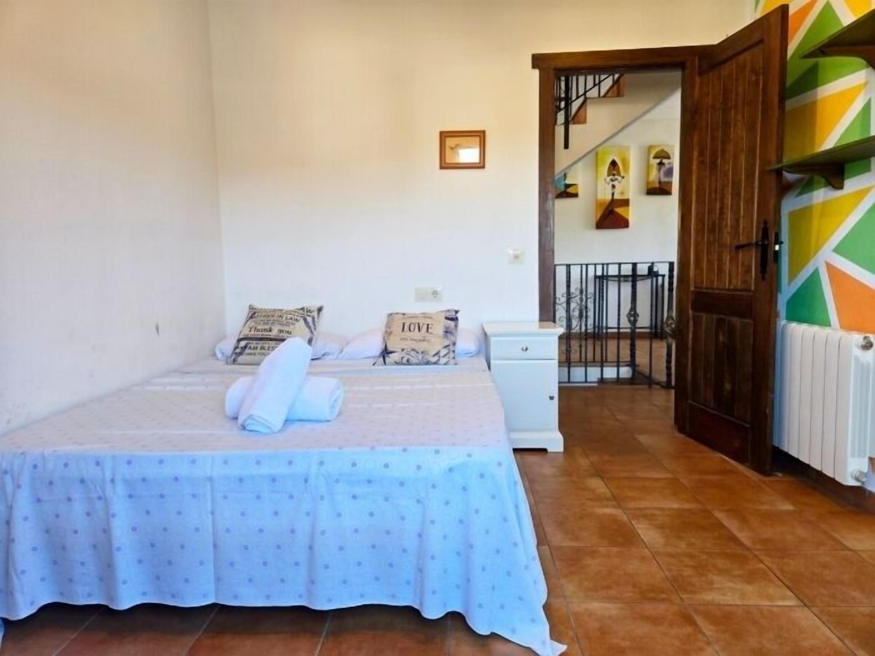 A bedroom with a bed, pillows, a nightstand, a radiator, and a staircase leading to another room.