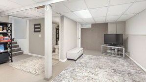 A home entertainment room with a TV on a glass stand, a white bench, and a carpeted floor. - 4.2 mi - TBK Sports Complex, 8.6 mi - Airport (Bettendorf)