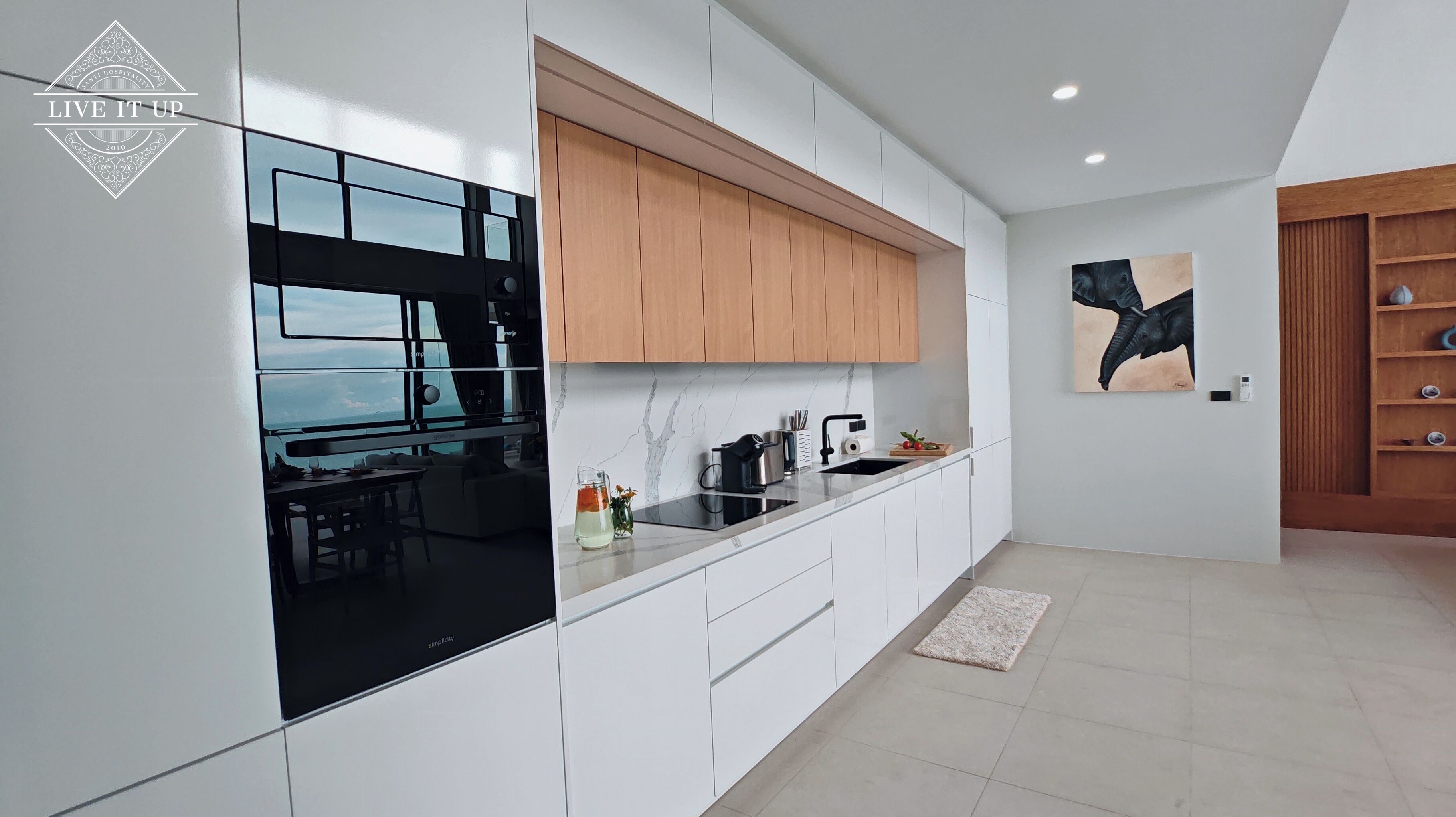 A modern kitchen with white cabinetry, a black countertop, and a wooden upper cabinet.