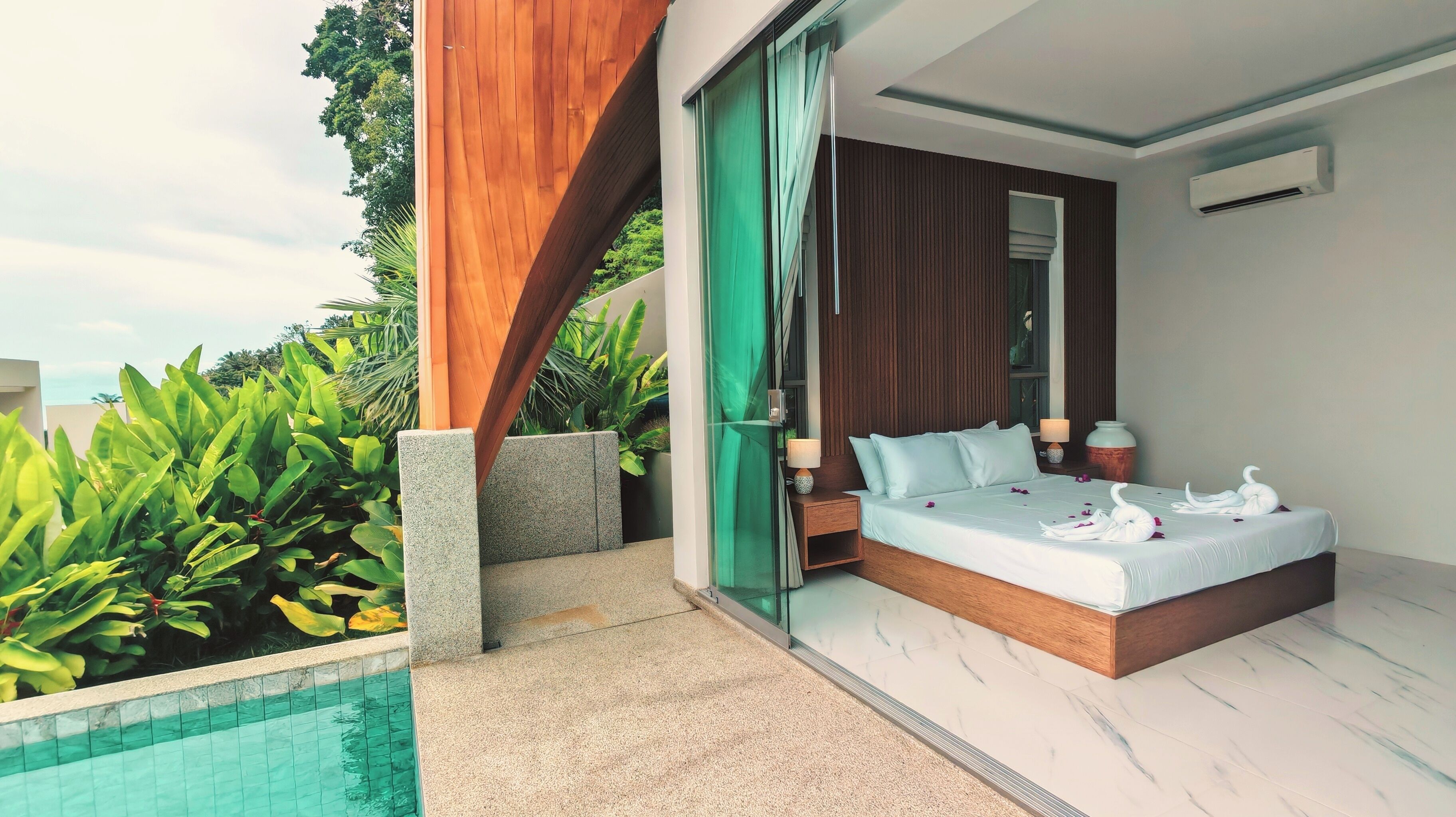 Quarto moderno com uma cama grande, uma mesa de cabeceira, um abajur e vista para uma piscina.