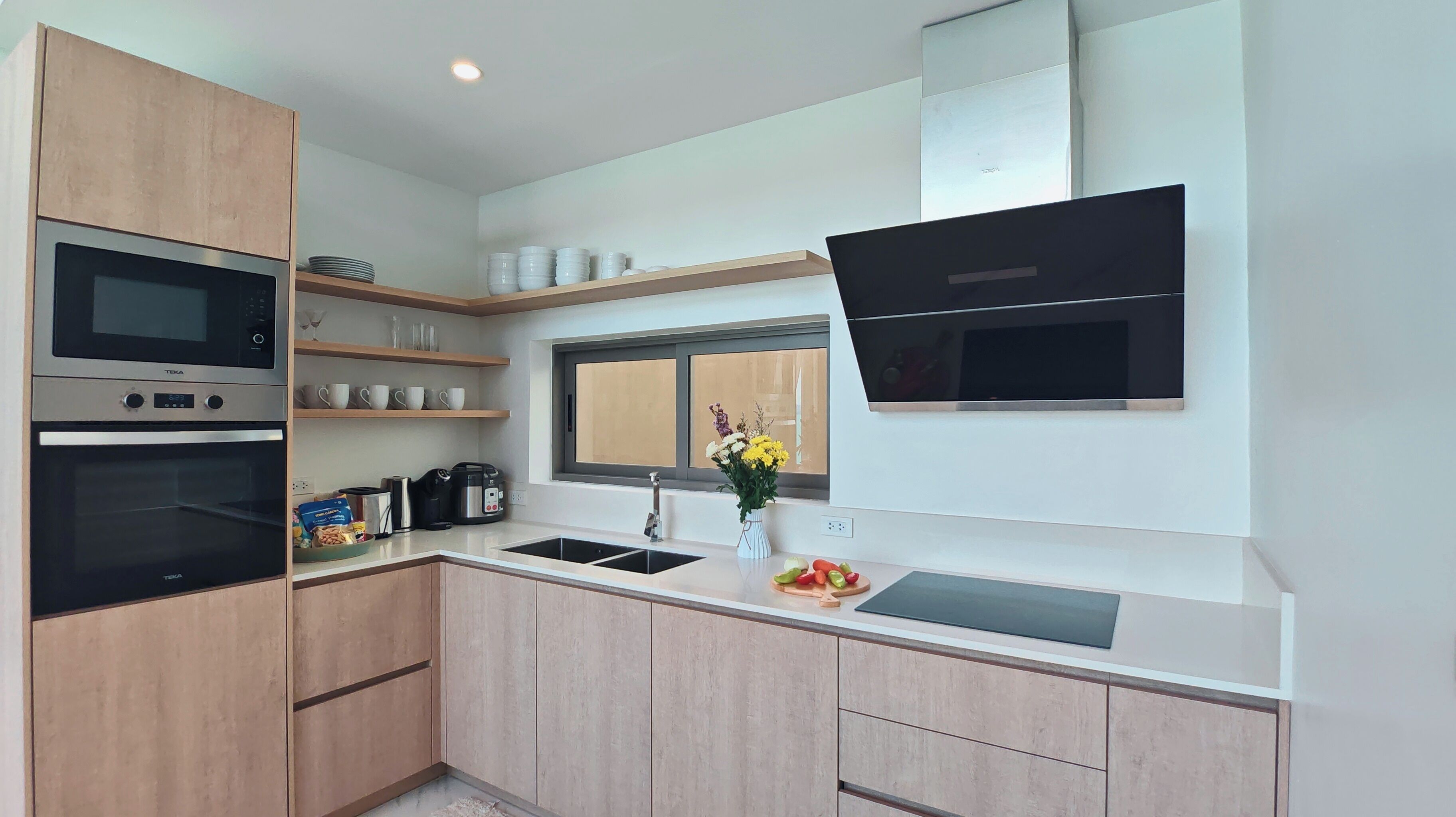 A modern kitchen with built-in appliances, wooden cabinets, and a window with a flower arrangement.