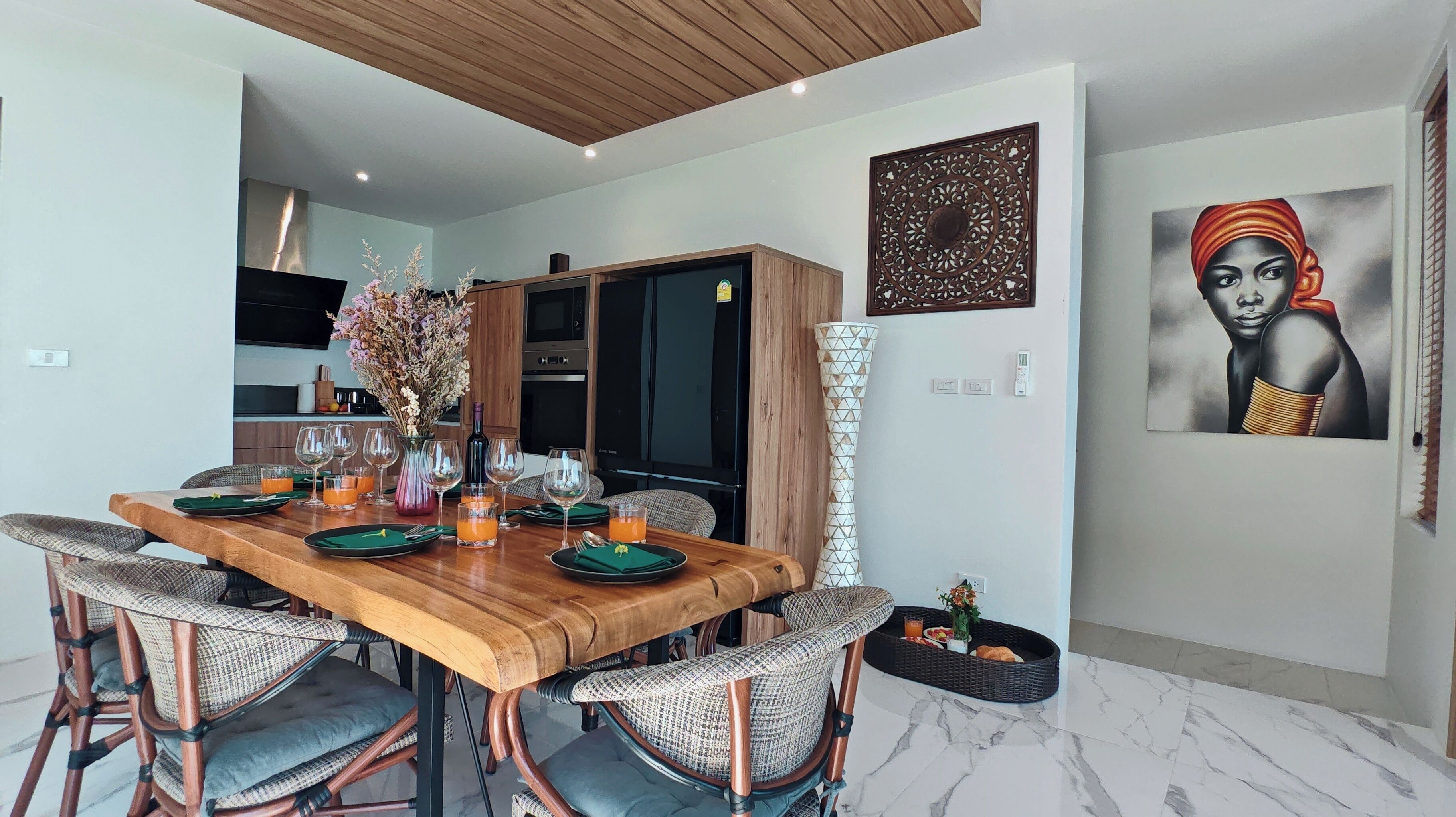 A modern dining area with a wooden table set for six, surrounded by wicker chairs.