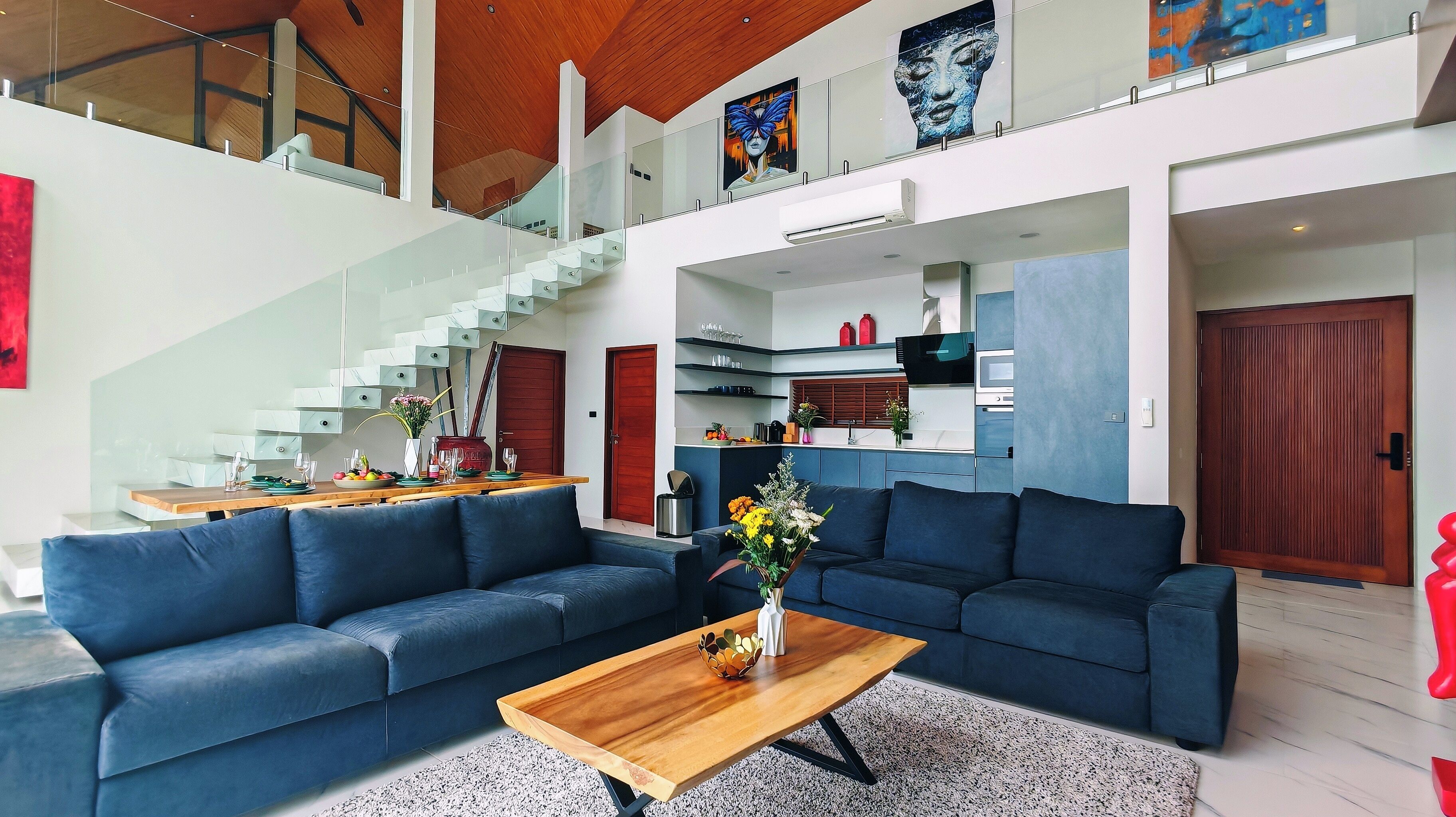 Un vaste espace de vie comprenant un canapé bleu, une table basse en bois et un escalier menant à un niveau supérieur.