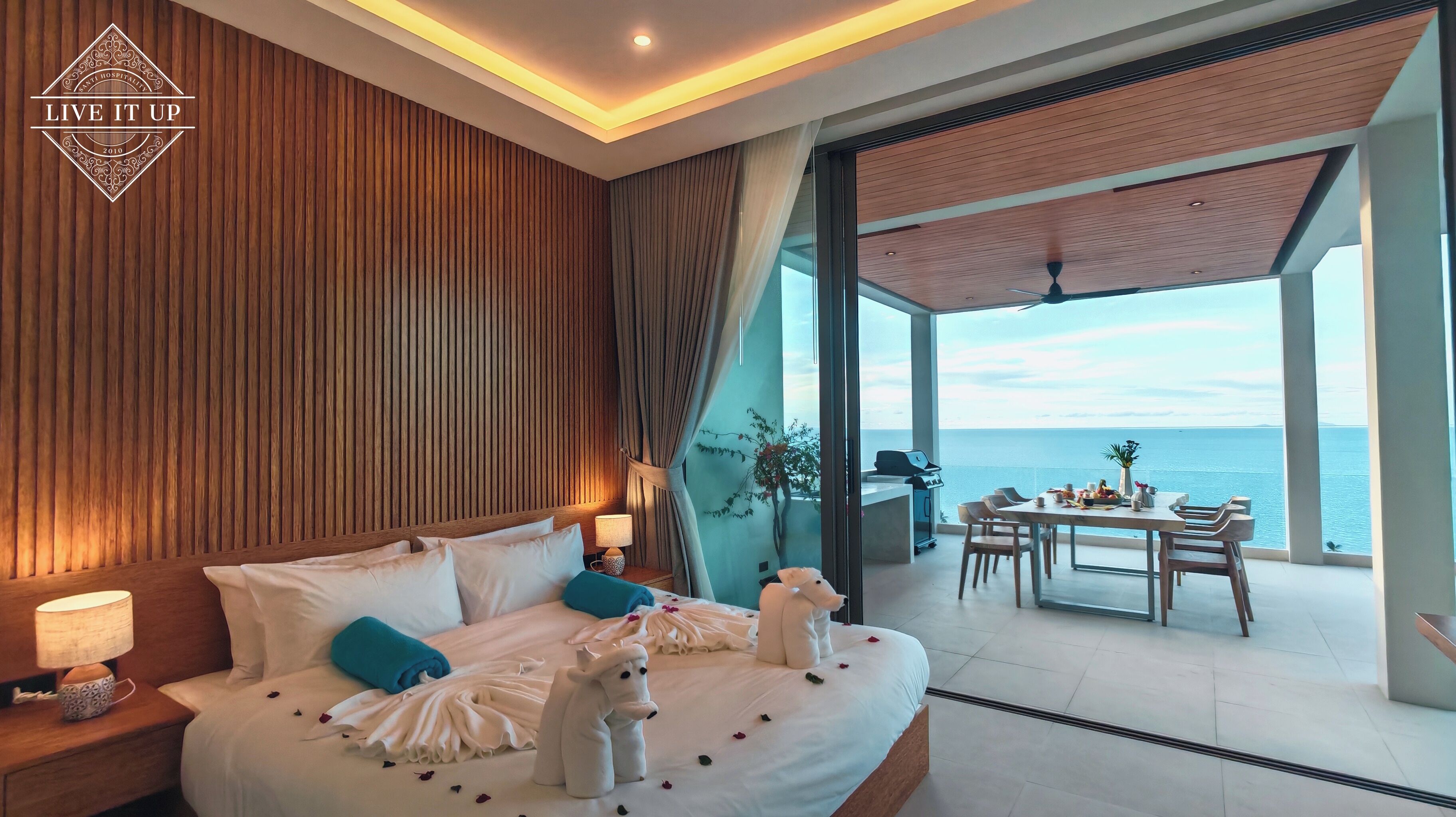 Ein modernes Hotelzimmer mit einem großen Bett, einem Balkon mit Meerblick und einem Essbereich mit Tisch und Stühlen.