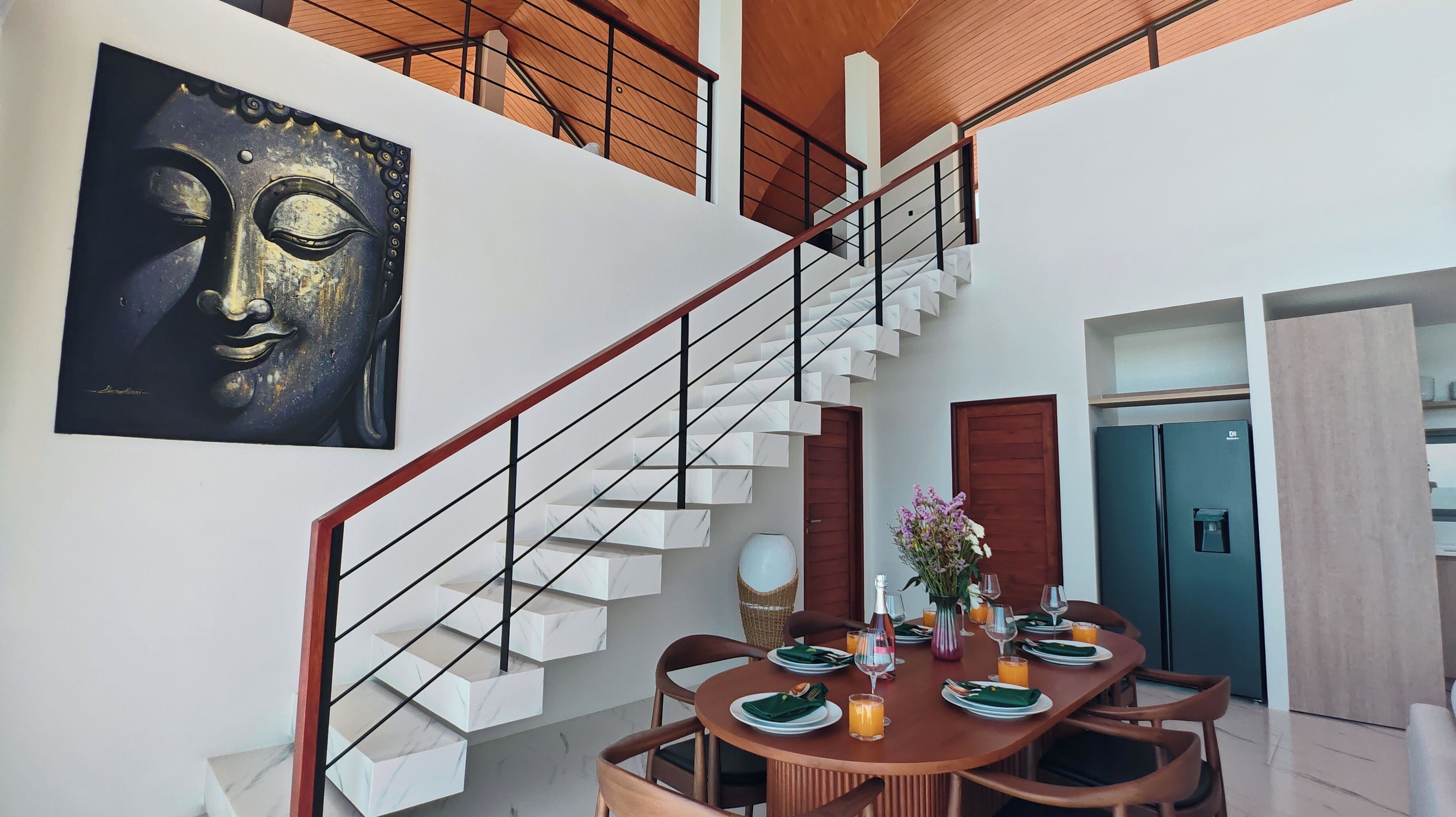 A modern dining area with a marble staircase, a dining table set for four, and a Buddha painting on the wall.