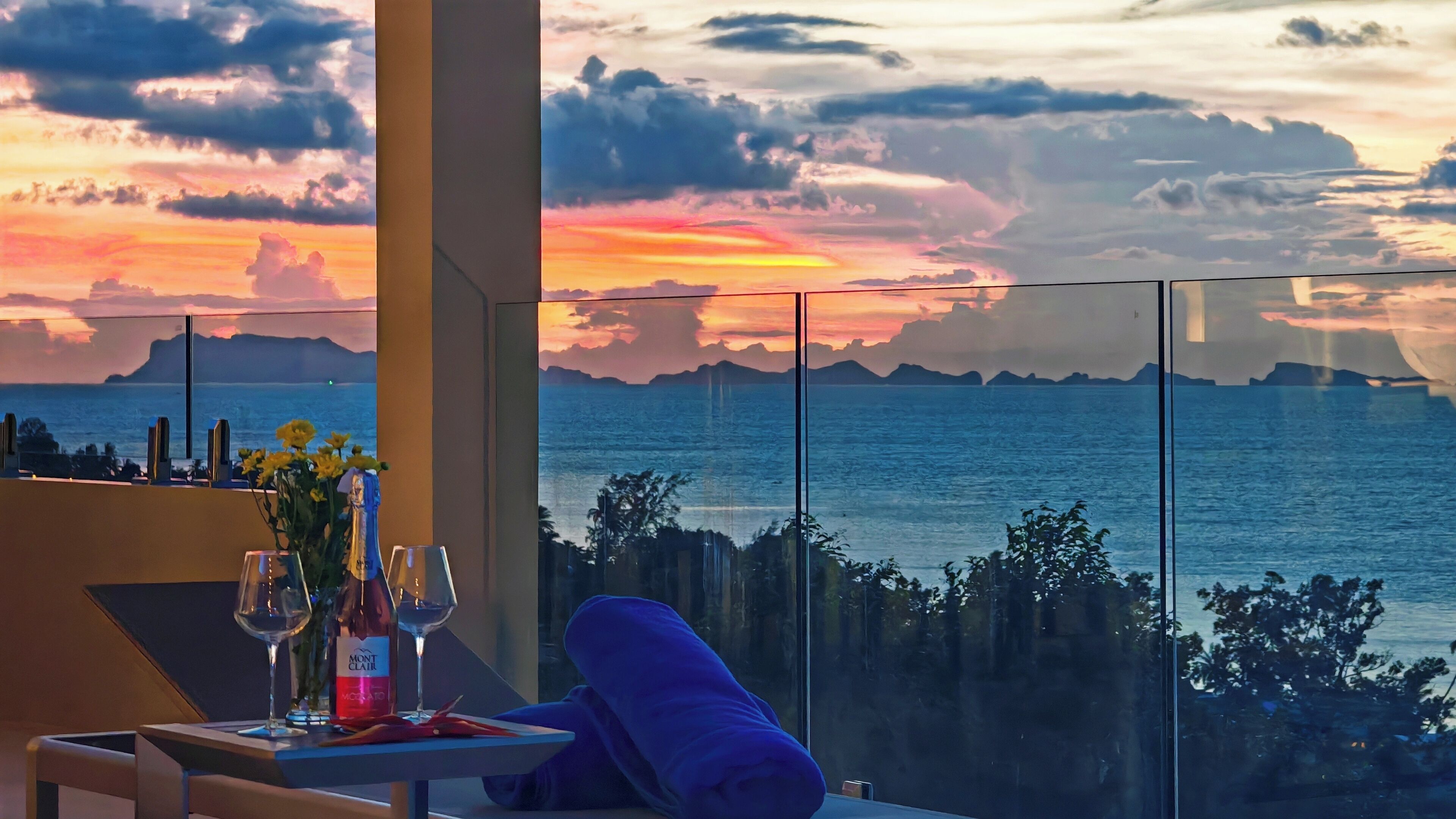A table with a bottle of Mont Blanc wine, two wine glasses, and a vase with yellow flowers.