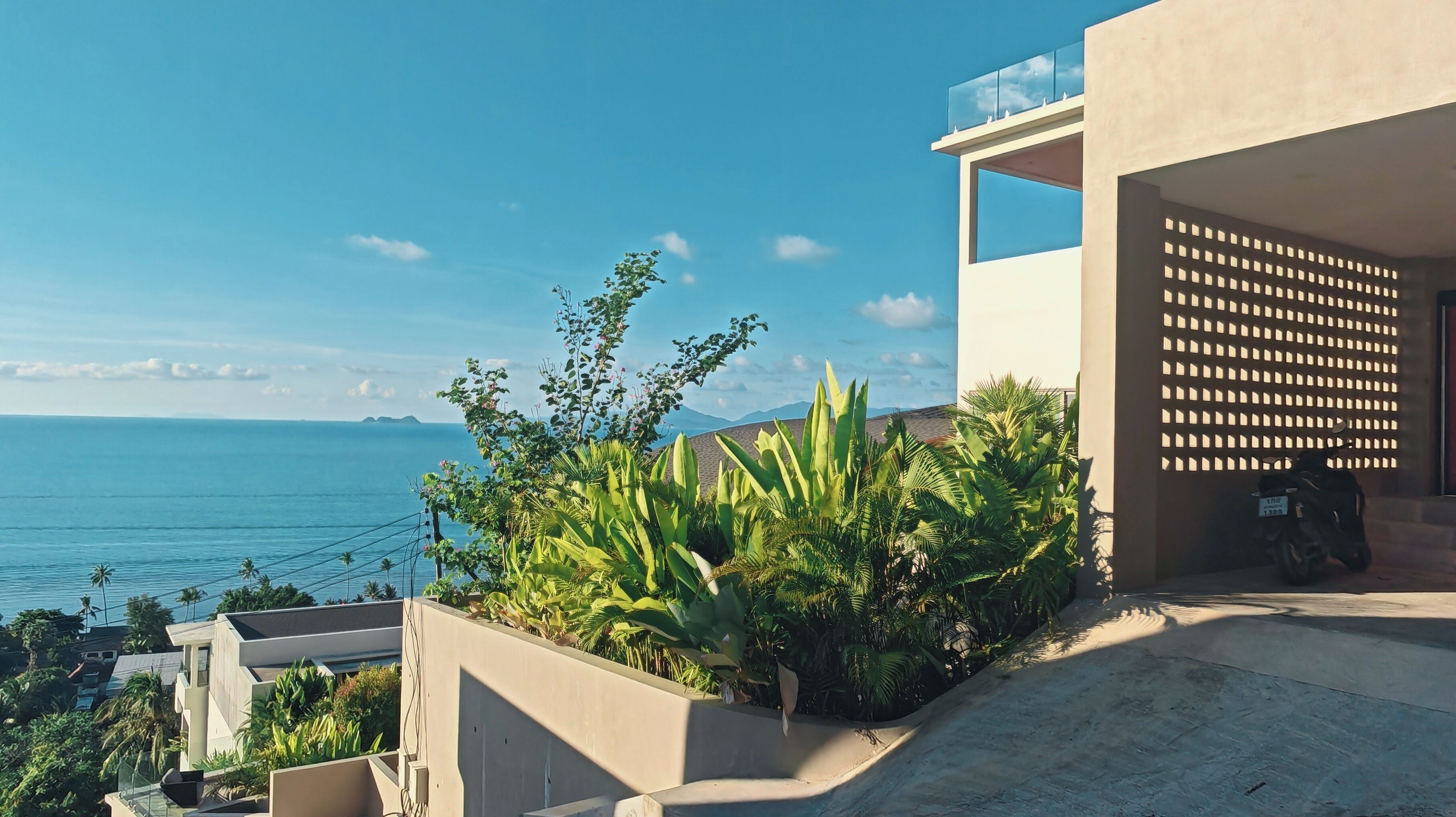 A modern building with a view of the sea, surrounded by lush greenery.
