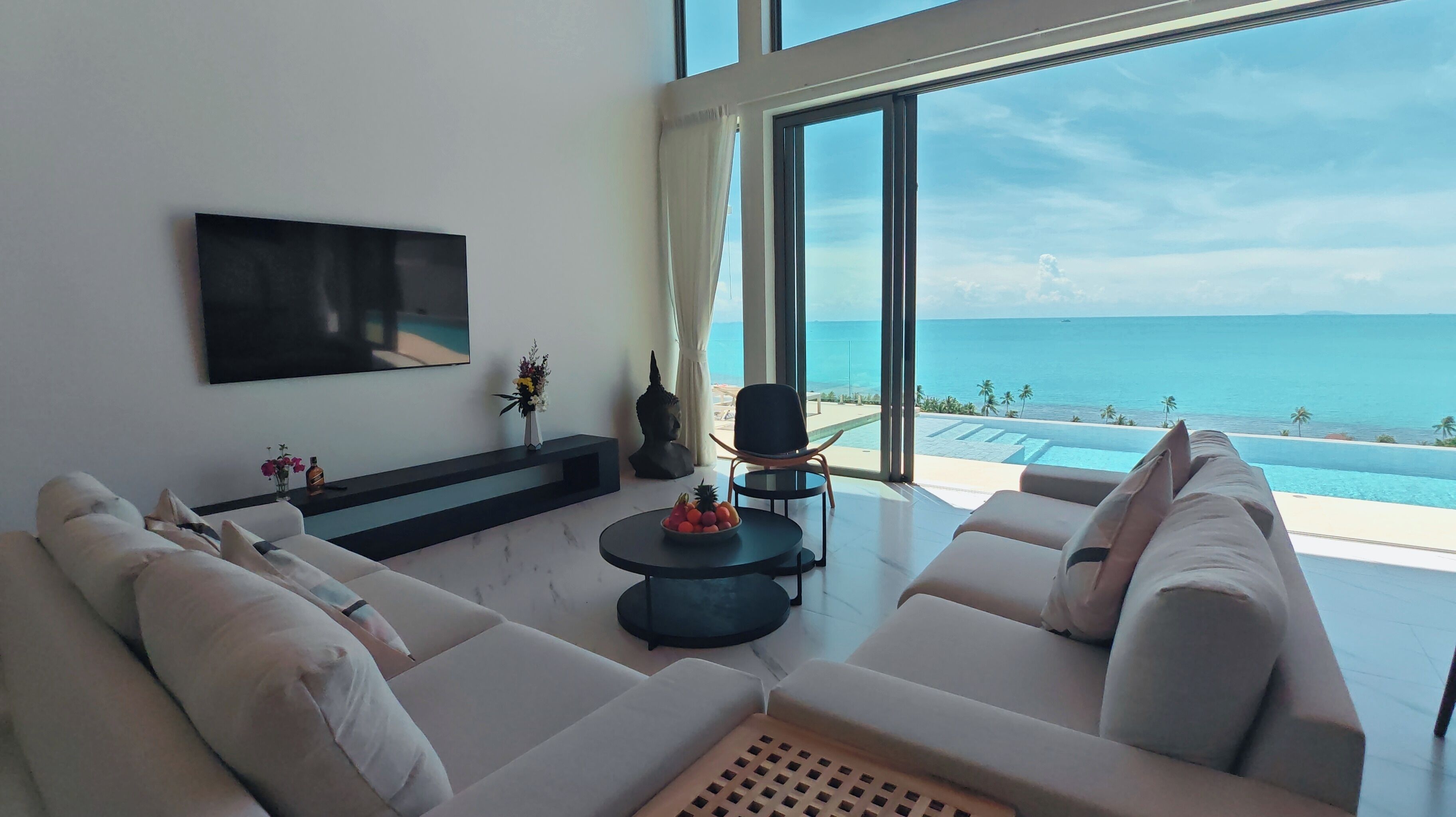 Een moderne woonkamer met een grote bank, een salontafel en een flatscreen televisie aan de muur. Grote ramen bieden uitzicht op de oceaan.