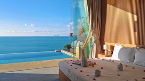 A bedroom with a large bed, a bedside table with a lamp, and a view of the ocean. - Santi Pura Villas (Koh Samui)