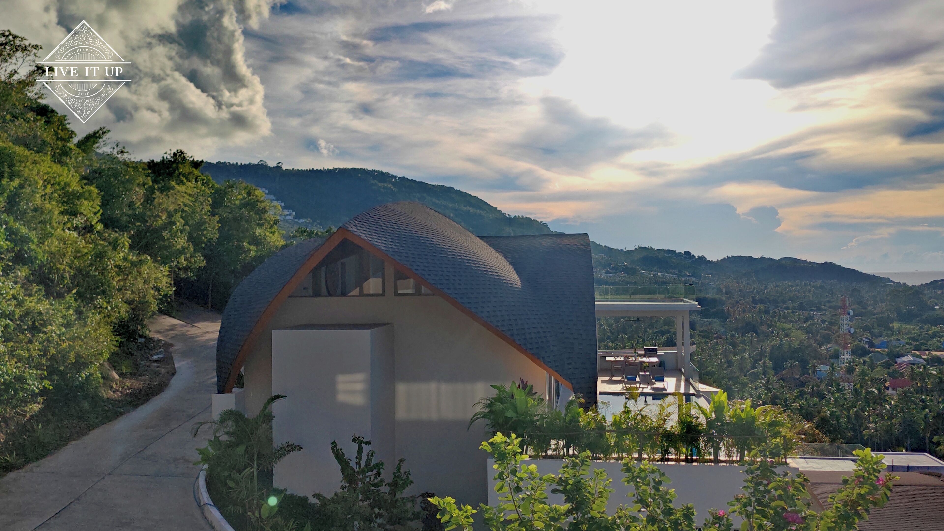 Une maison moderne avec un toit en pente, un grand garage et un balcon doté d’un espace salon extérieur.