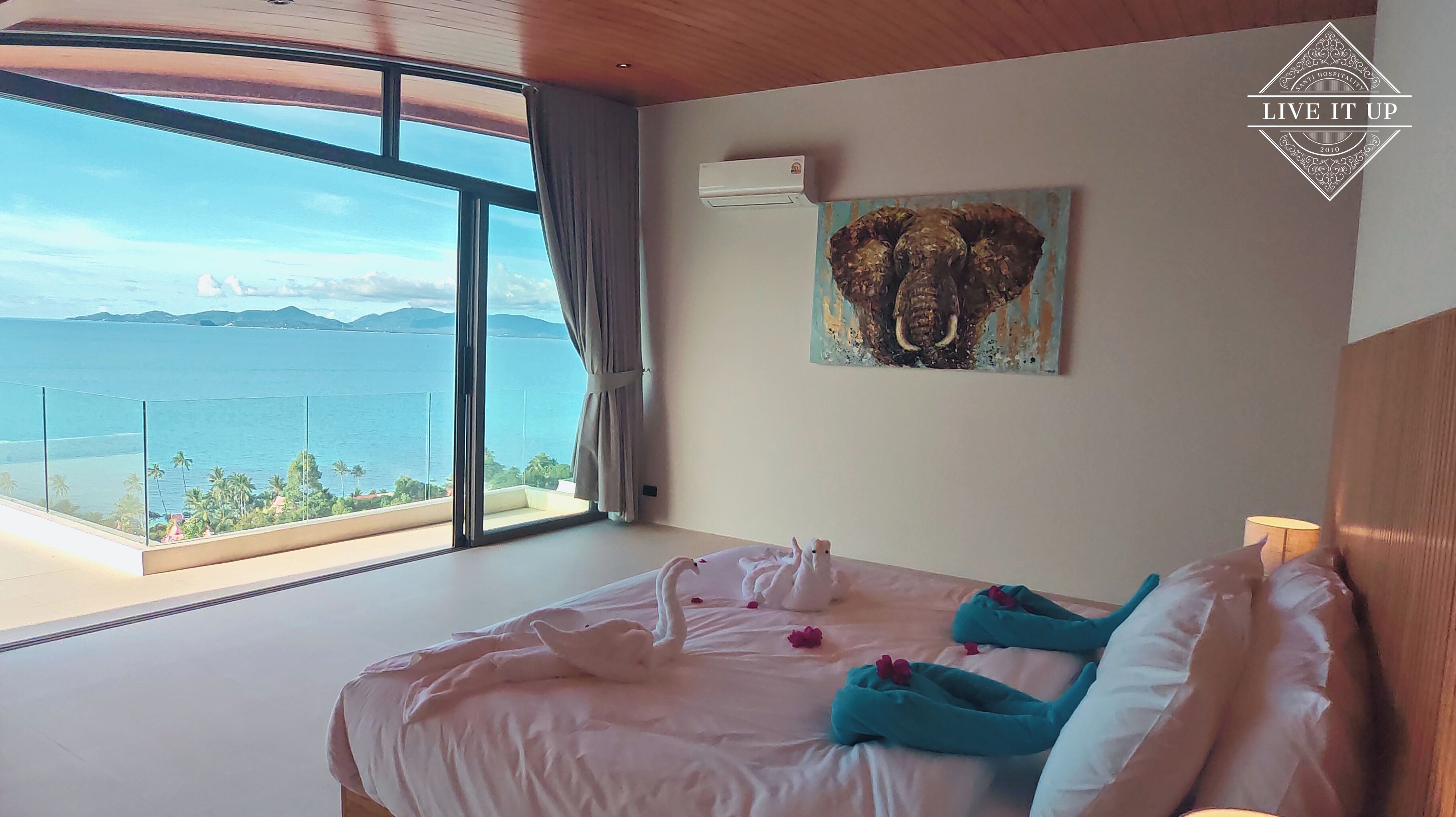 Een slaapkamer met een groot bed, een oliefje van een olifant en uitzicht op zee.