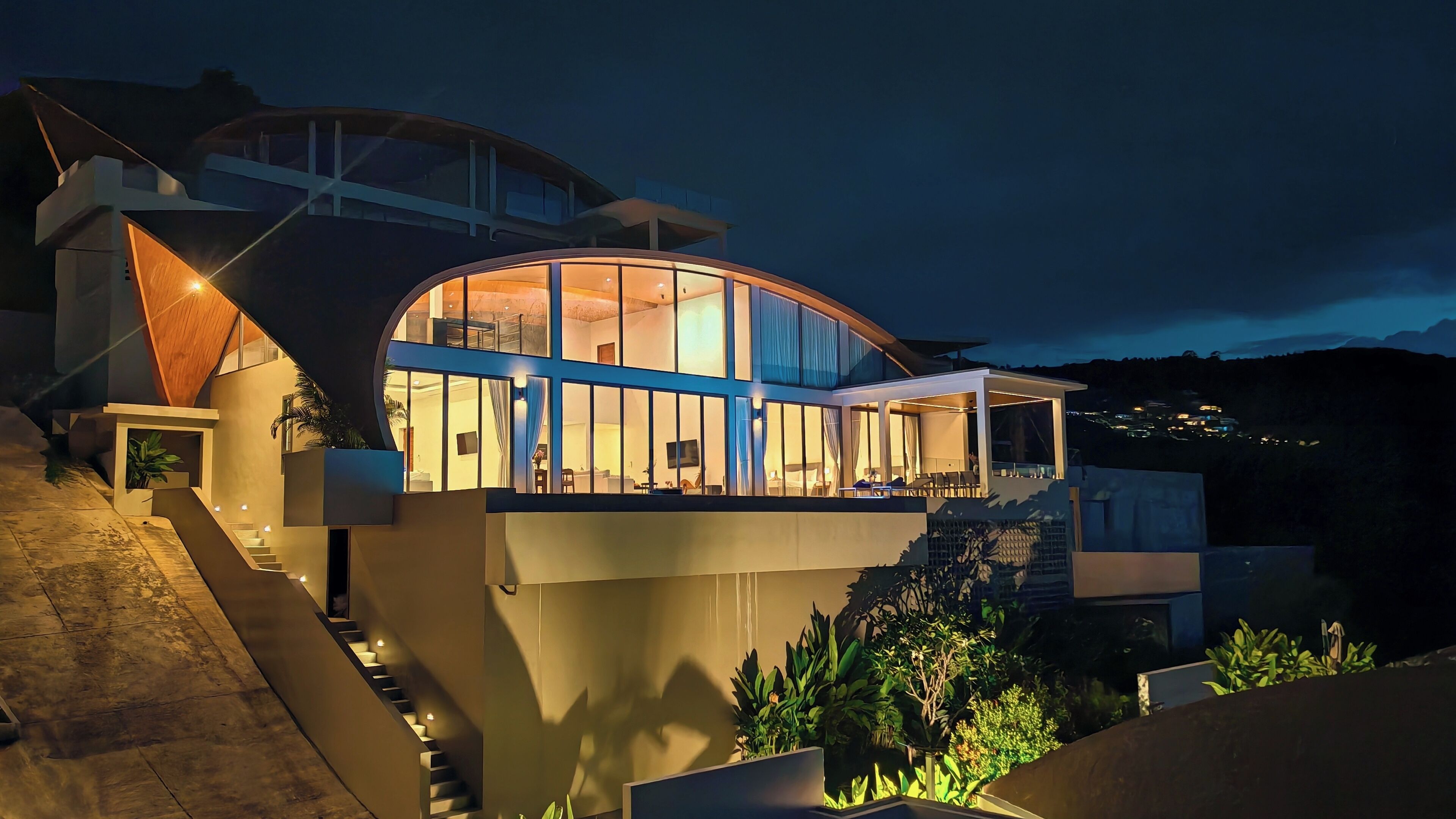 Uma casa moderna com fachada de vidro curvo, escada visível e varanda.