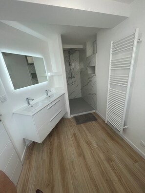 Features a sleek vanity with dual sinks and a shower area with a marble backsplash.