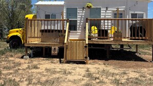 Una casa móvil con terraza de madera, un porche pequeño y un vehículo estacionado cerca.