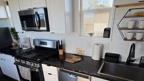 Una cocina moderna con armarios blancos, electrodomésticos de acero inoxidable y un ventanal que deja entrar luz natural.