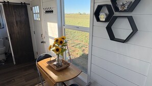 Un comedor con una mesa de madera, una silla y un jarrón con girasoles junto a una ventana que da a un campo.