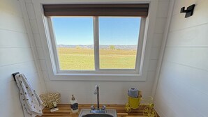 Cocina compacta con encimera de madera, un lavamanos y una ventana con vistas a un campo.
