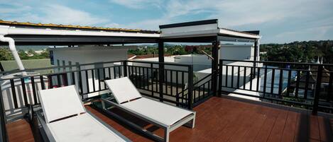 Una terraza de madera con dos tumbonas blancas y un área de estar cubierta.