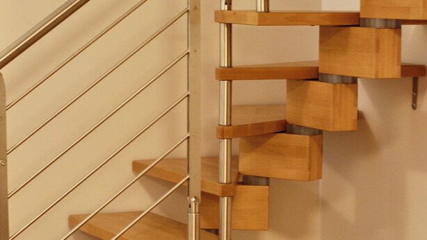 Un escalier moderne en bois, doté de rampes en métal et agrémenté d’un pot en céramique décoratif posé sur le sol.