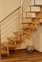Una escalera de madera moderna con barandillas de metal y una maceta decorativa de cerámica en el suelo.