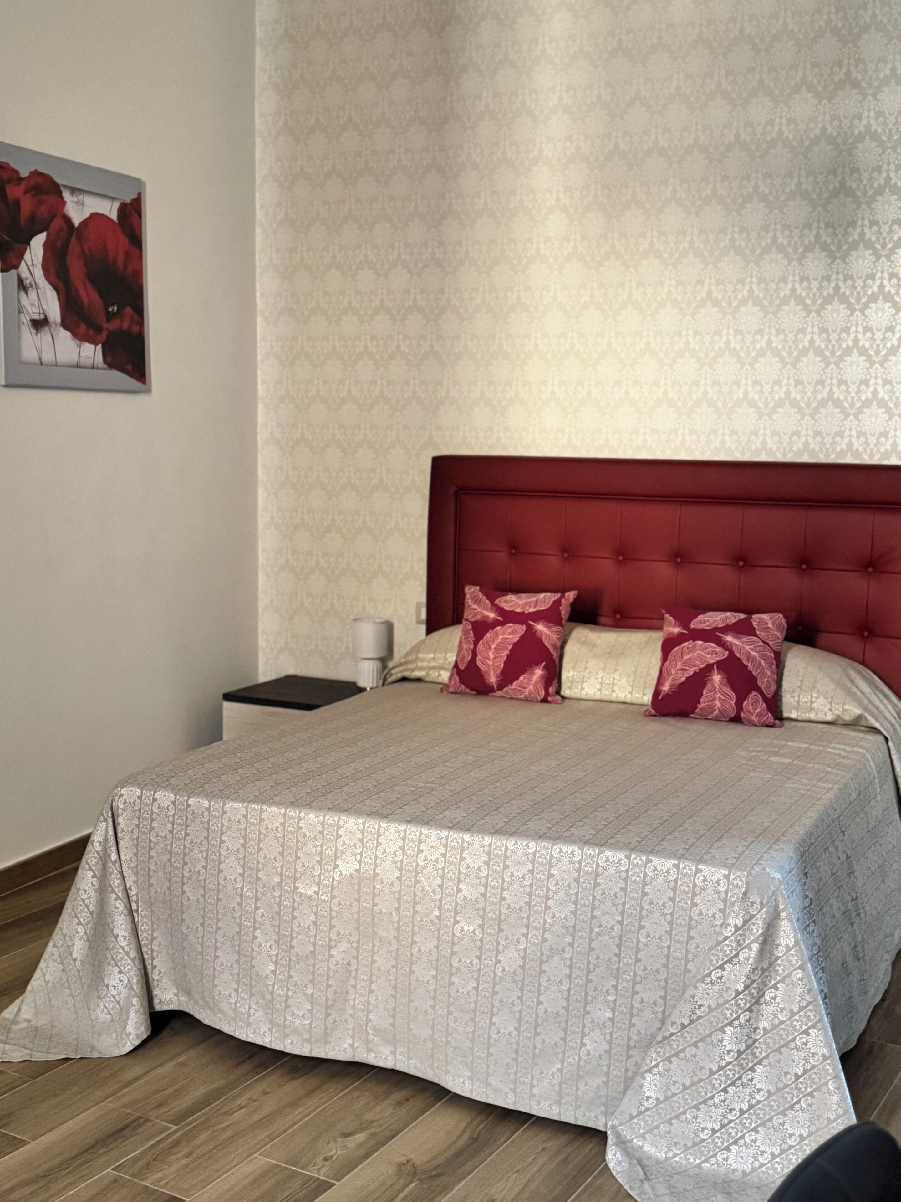 A neatly made bed with a patterned bedspread, a red upholstered headboard, and two decorative pillows.