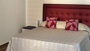A neatly made bed with a patterned bedspread, a red upholstered headboard, and two decorative pillows.