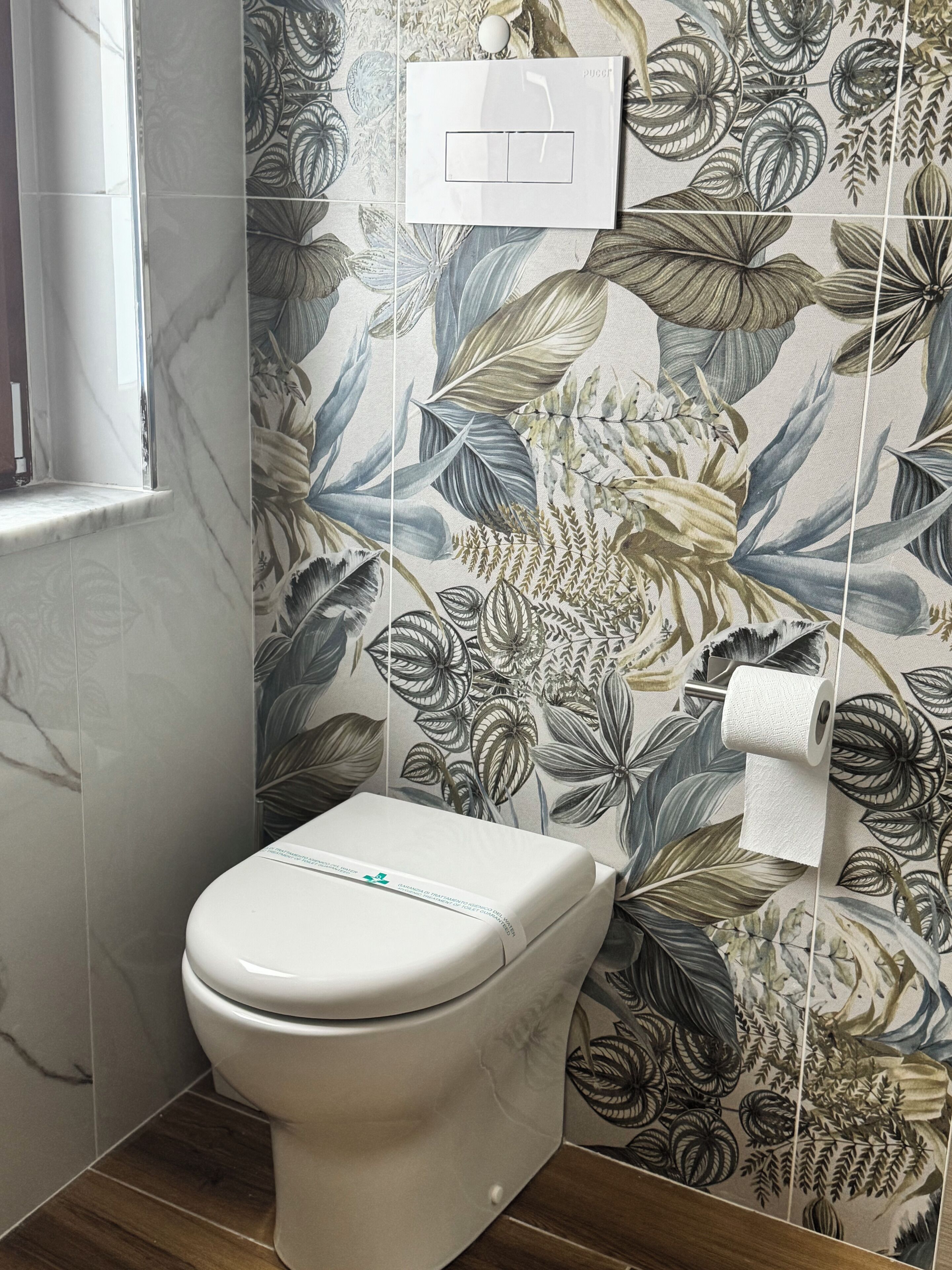 A bathroom with a toilet, a wall-mounted light switch, and a toilet paper holder.