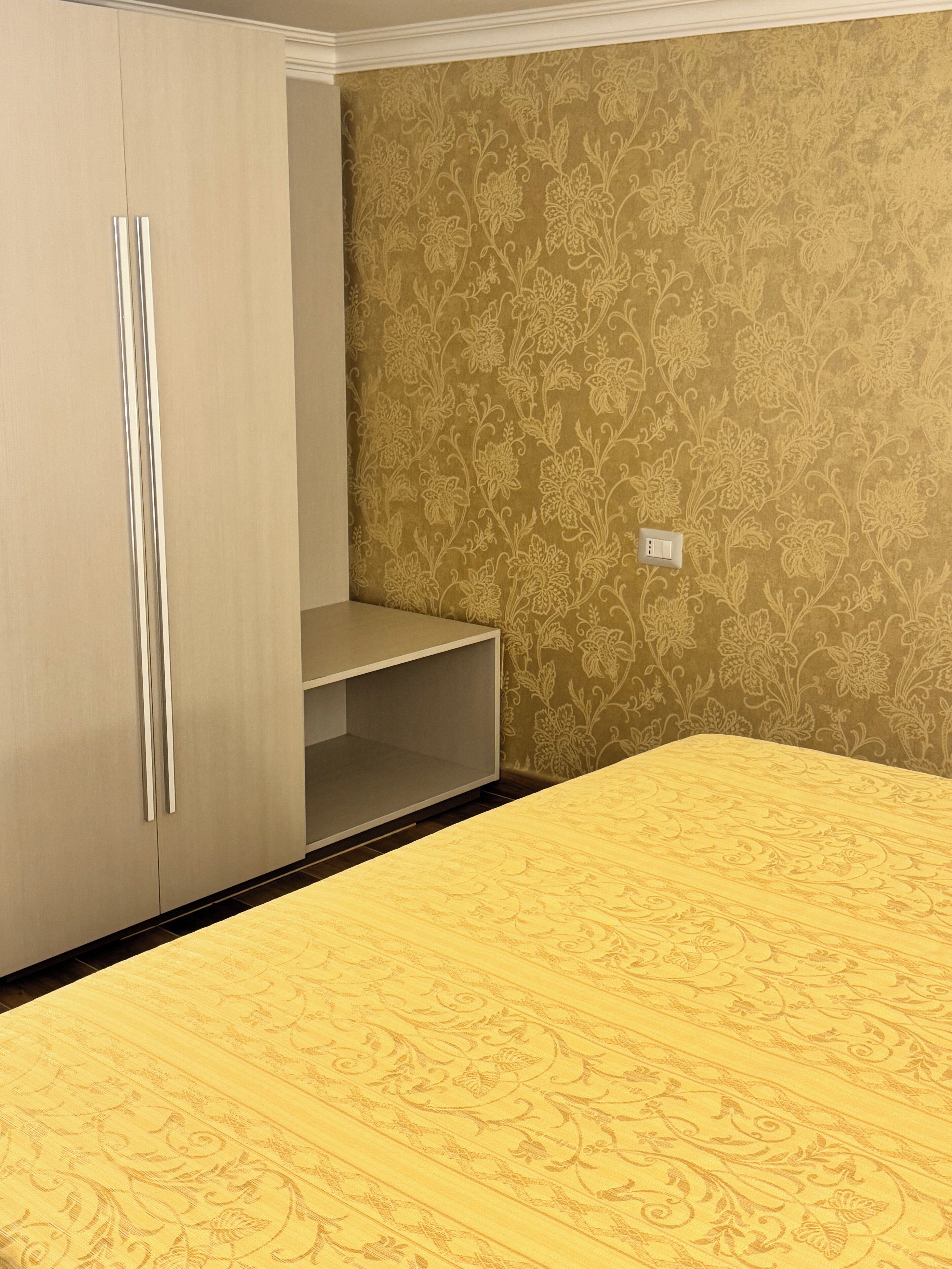 A room with a bed, wardrobe, and patterned wallpaper.