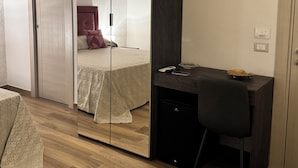 Une chambre avec une armoire à miroir, un lit avec une literie à motifs, un bureau avec une chaise et une petite table sur laquelle sont posés divers objets.