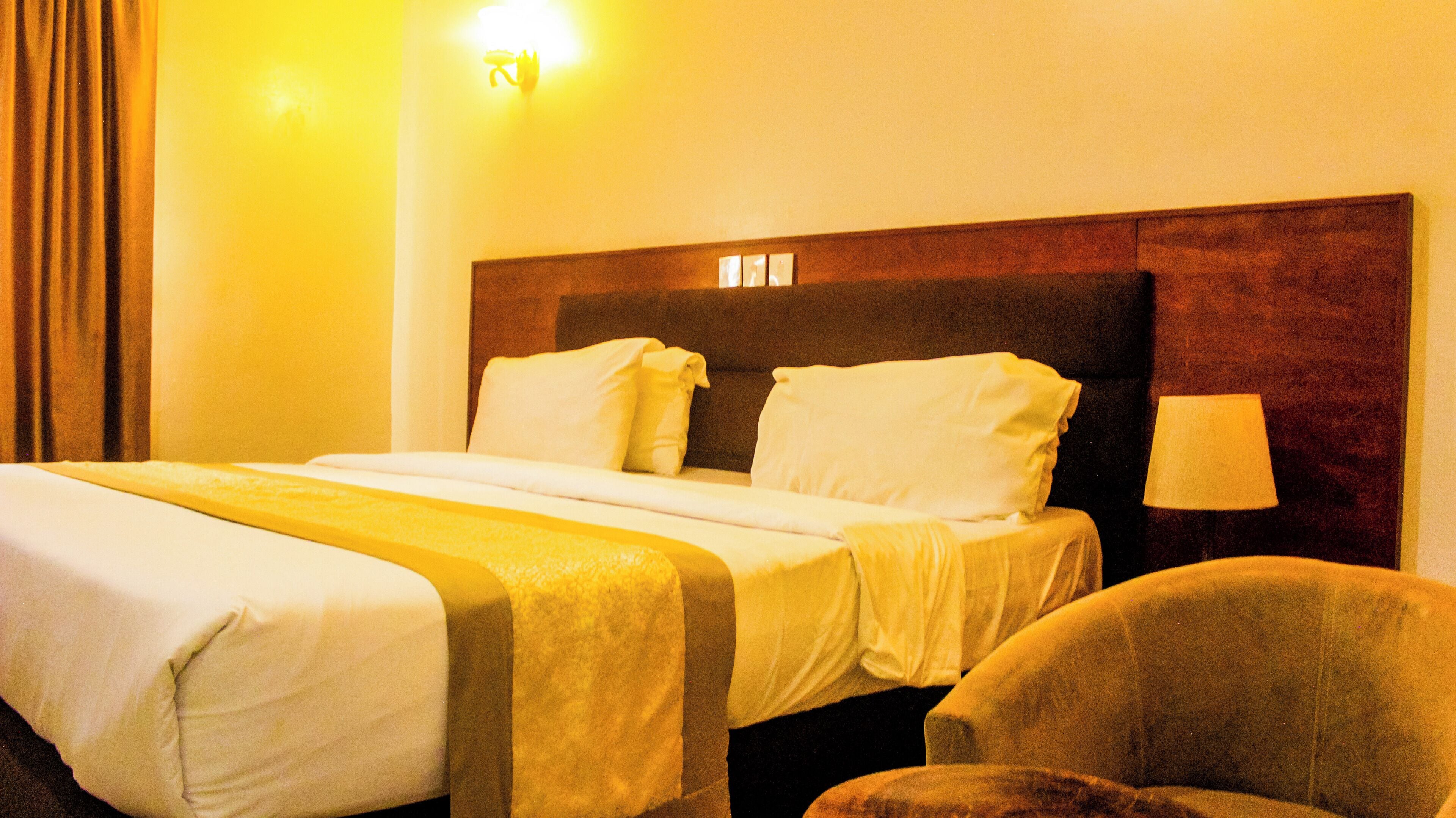 Una camera d'albergo con un letto grande, una testiera in legno, una lampada da comodino e una sedia.