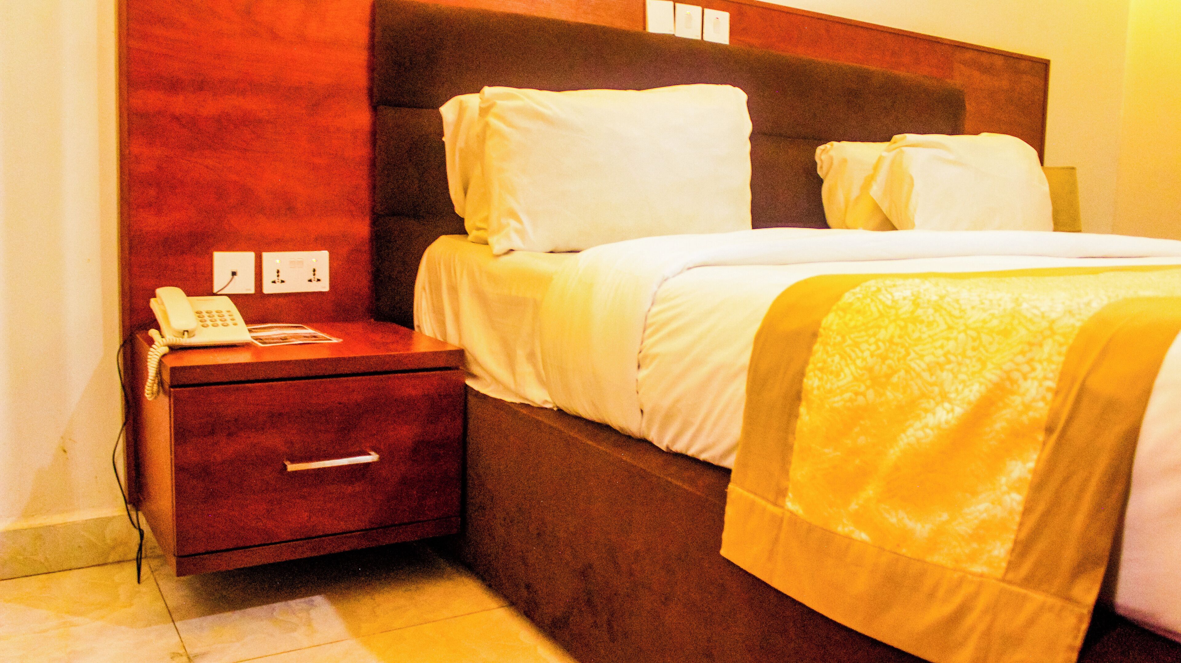 Une chambre d’hôtel avec un lit, une table de chevet avec un téléphone et une prise électrique au mur.