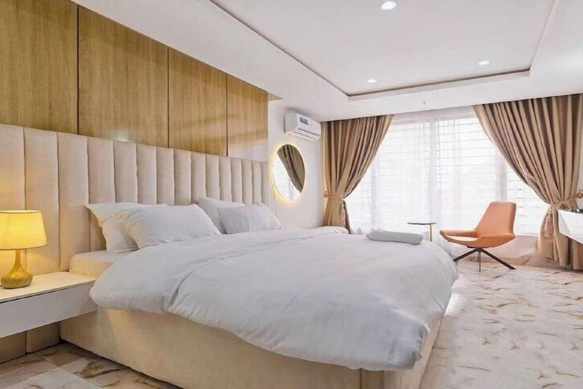 A modern hotel room with a large bed, a bedside lamp, a desk, a chair, and a TV.