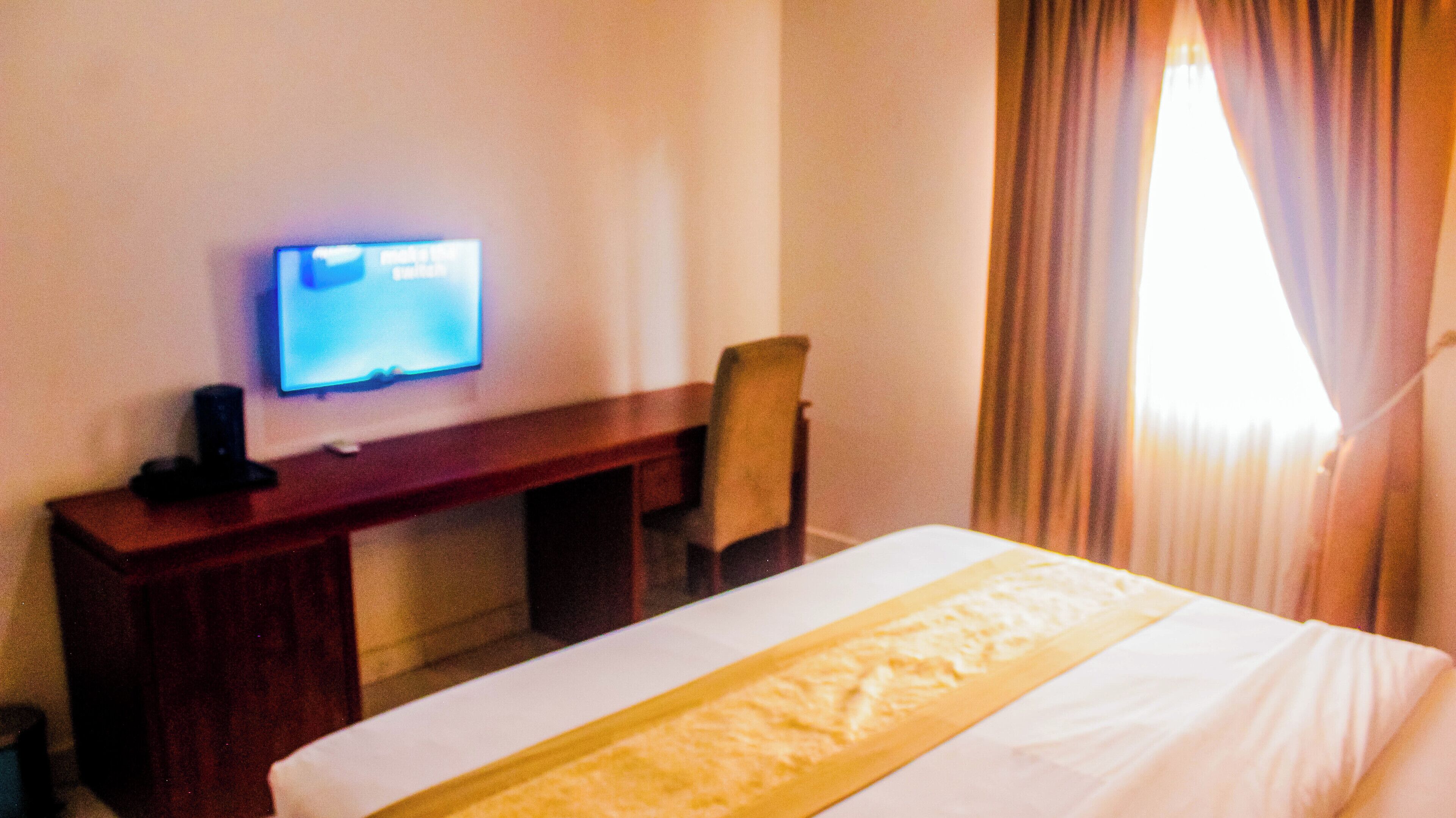 Une chambre d’hôtel équipée d’un lit, d’un bureau, d’une chaise, d’une télévision et d’une fenêtre avec des rideaux.