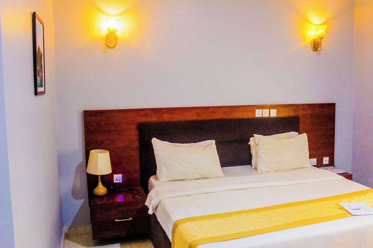 A hotel room with a large bed, two bedside tables, a nightstand, and wall-mounted lights.