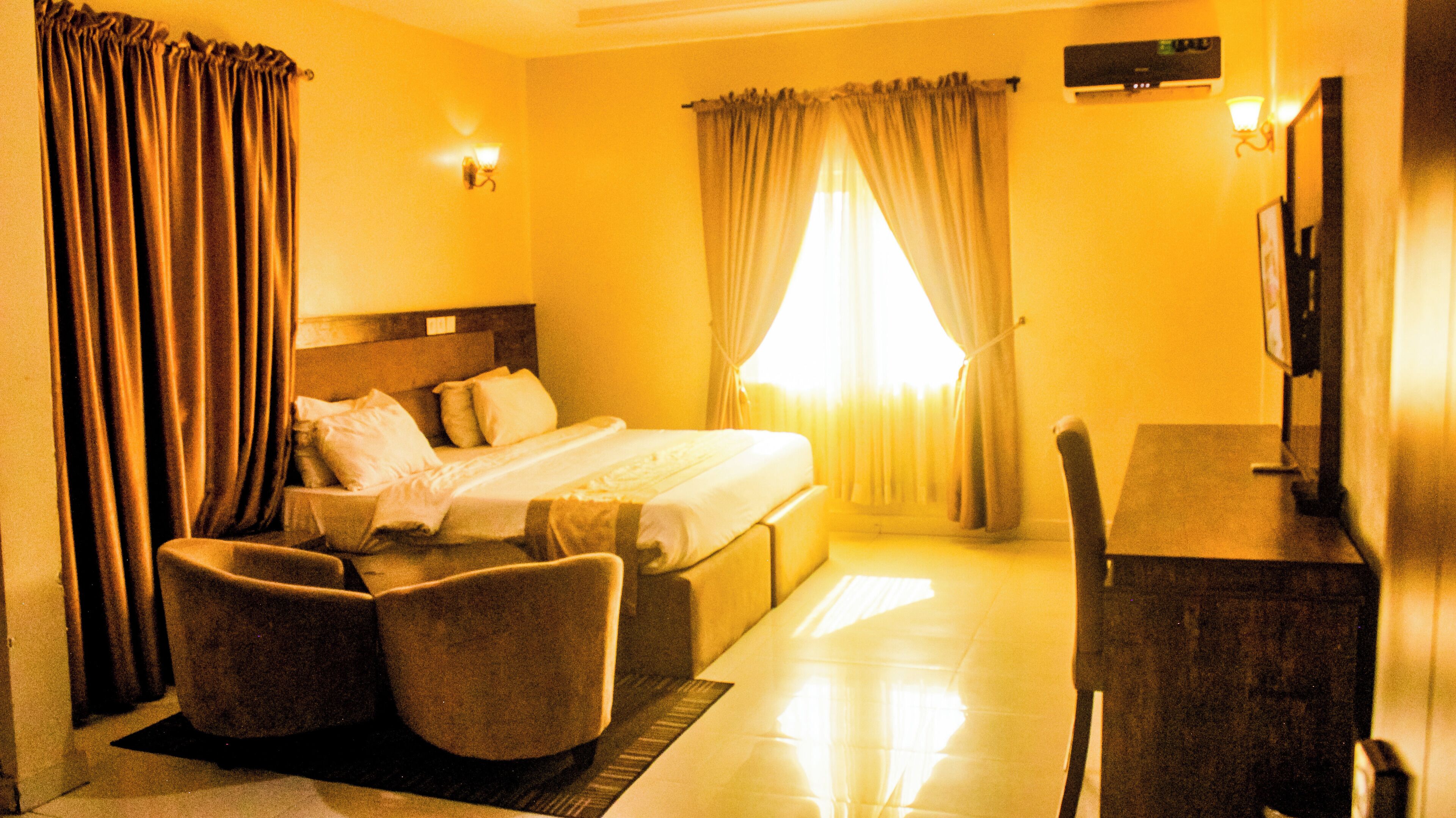 A hotel room with a bed, two armchairs, a desk, a TV, and curtains.