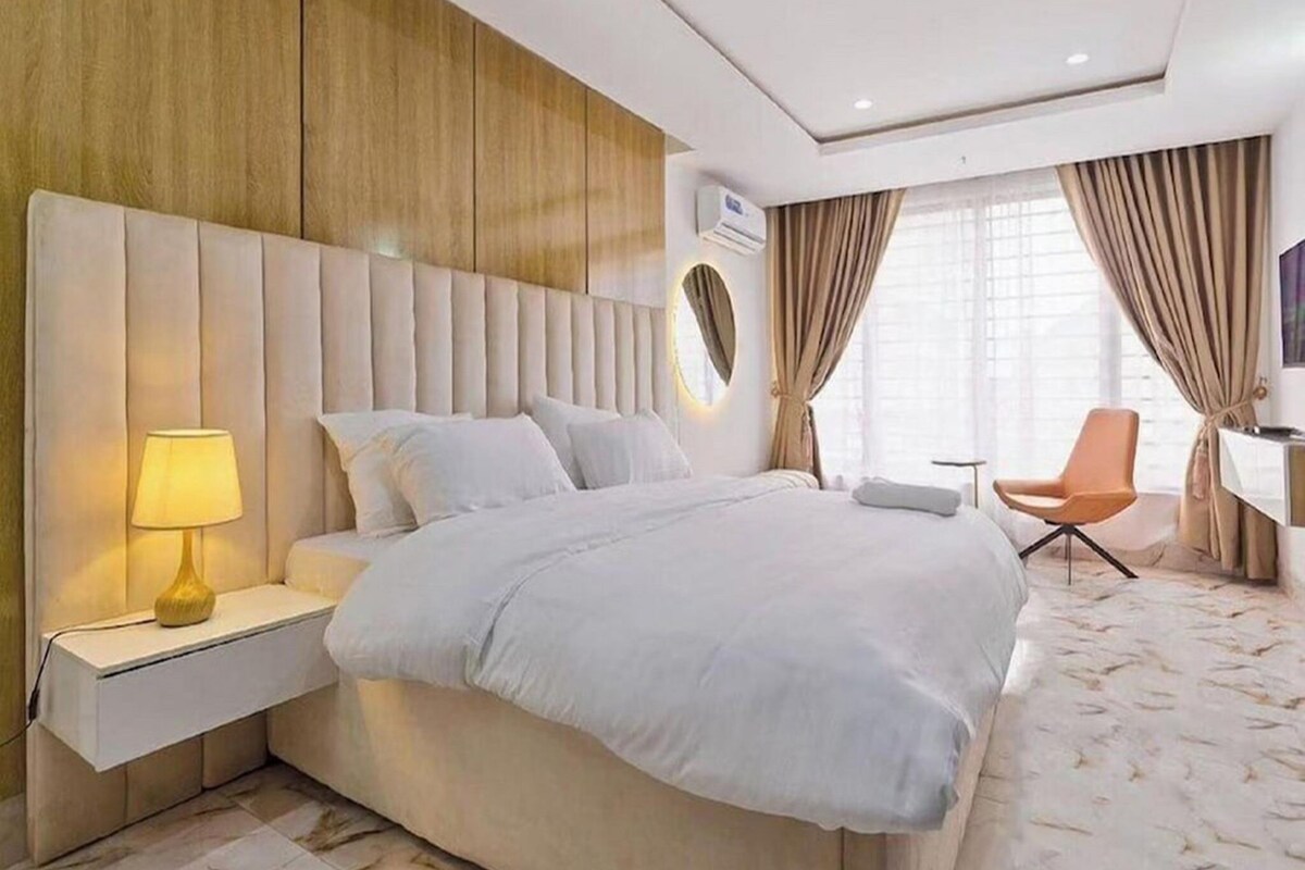 Une chambre d’hôtel moderne avec un grand lit, une table de chevet avec une lampe, un bureau avec une chaise et un téléviseur.