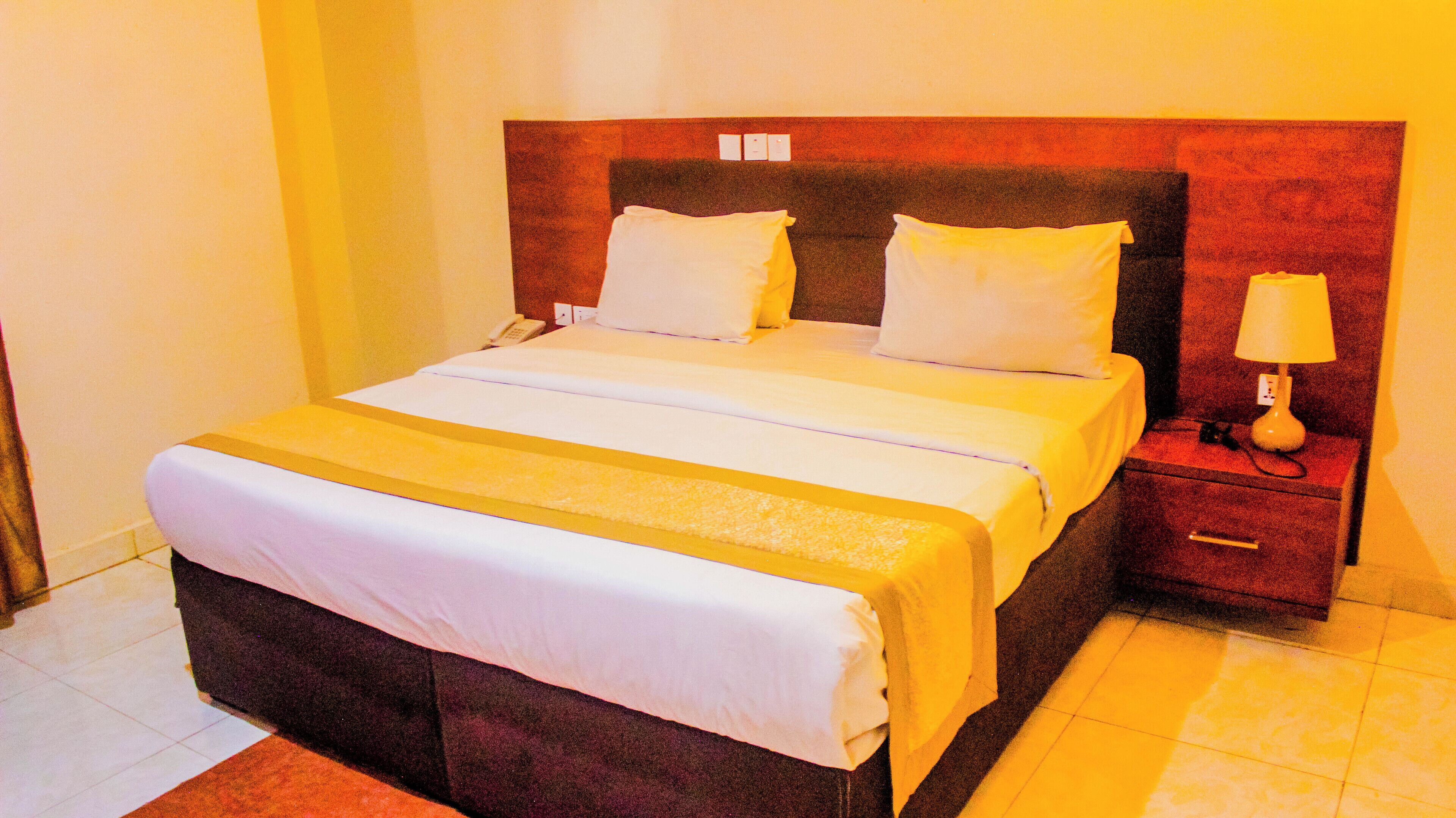 A hotel room with a large bed, two pillows, a bedside table with a lamp, and a telephone.